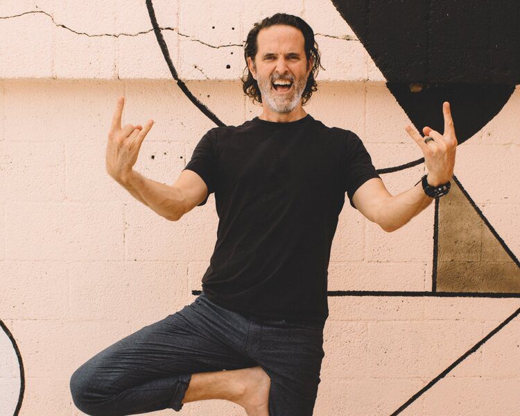 Yoga instructor and The Light Orchard founder Dalton Grant stands in Tree Pose (Vrksasana) with both hands doing the "sign of the beast" for added rock 'n' roll yoga charm.